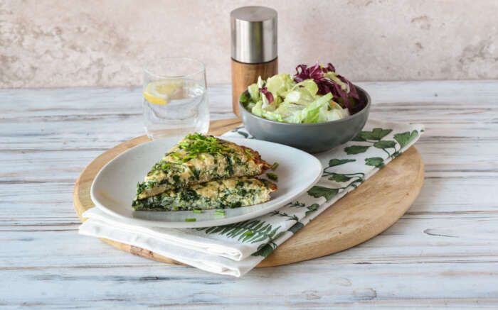 Zu sehen ist ein Teller mit einem Stück Tortilla, daneben ein kleiner Salat und ein Glas Wasser