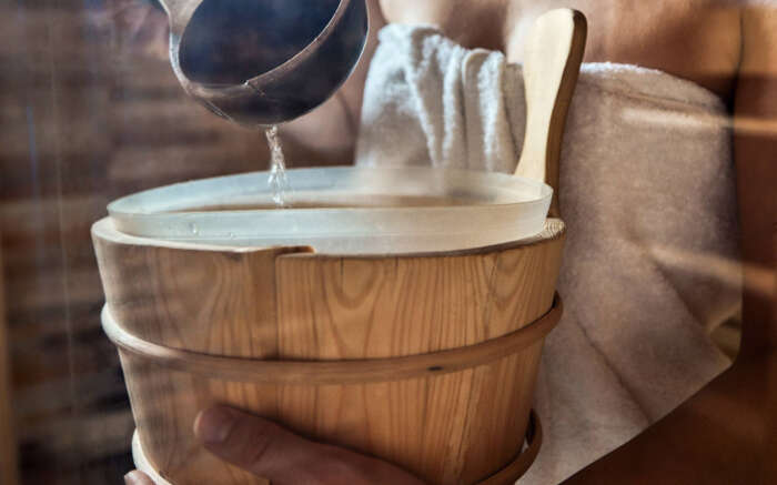 Eine Sauna, darin ein Fass,, in welches Wasser gegossen wird