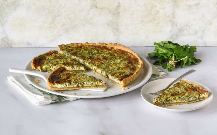 Auf einem grossen weissen Teller liegt eine Wähe, daneben ist ein Stück davon abgeschnitten auf einem kleinen Teller