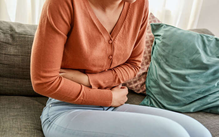 Eine Frau sitzt auf dem Sofa und hält sich den Bauch