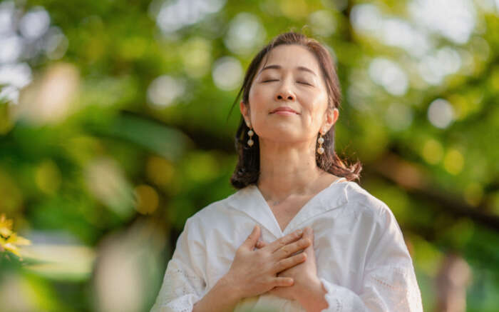 Eine Frau steht im Freien und atmet sichtbar aus und hält die Hände auf die Brust