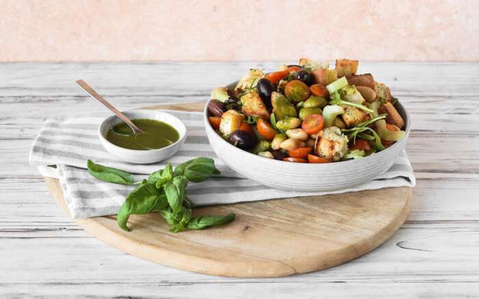 Eine Schüssel mit frischem Salat und Gemüse und einer kleinen Schale Salatsauce stehen auf einem Holzbrett