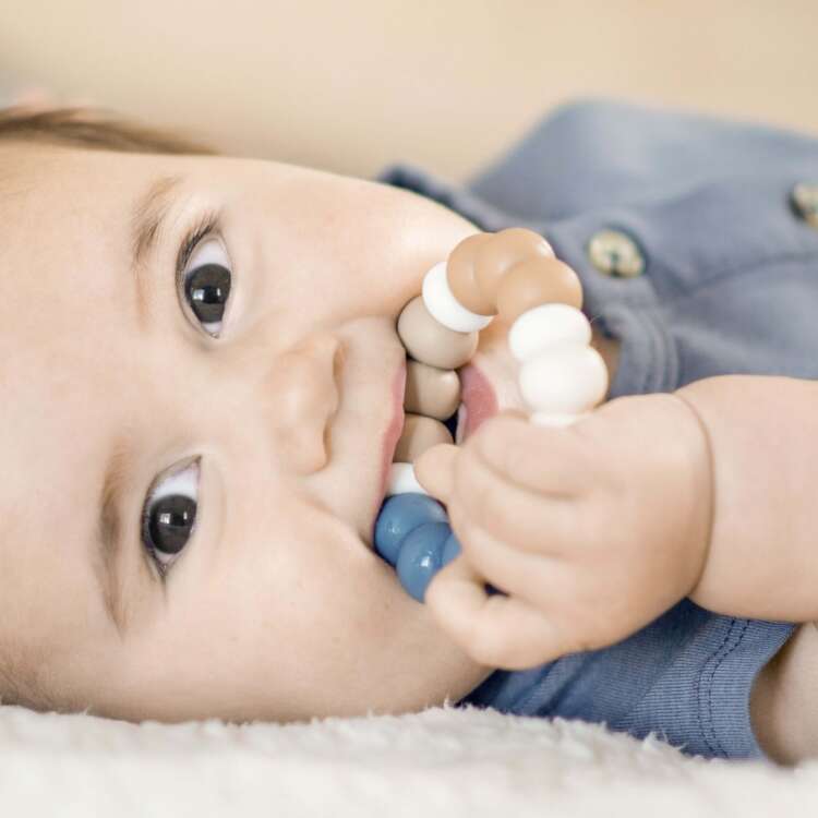 Baby liegt auf dem Rücken, schaut in die Kamera und kaut auf einem Beissring