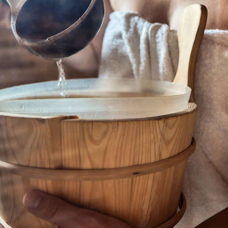 Eine Sauna, darin ein Fass,, in welches Wasser gegossen wird