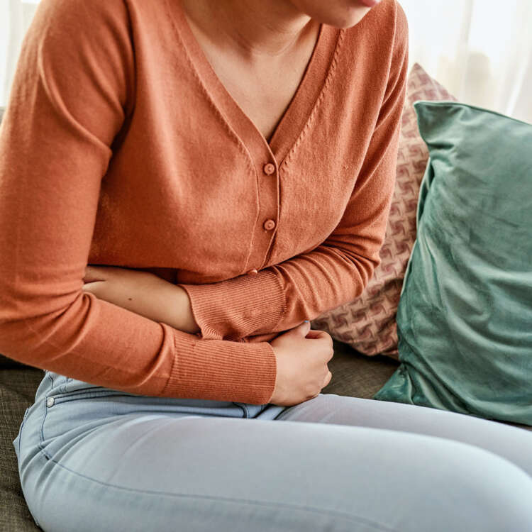 Eine Frau sitzt auf dem Sofa und hält sich den Bauch