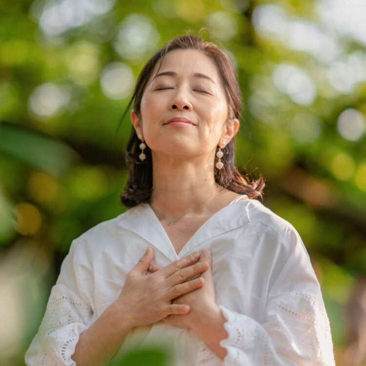 Eine Frau steht im Freien und atmet sichtbar aus und hält die Hände auf die Brust