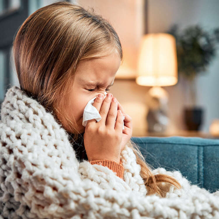 Ein Kind putzt sich die Nase, mit einer Wolldecke um den Körper