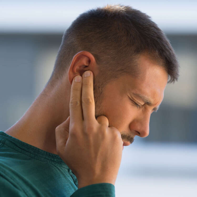 Person fasst sich mit schmerzverzerrtem Gesicht mit zwei Fingen an das rechte Ohr