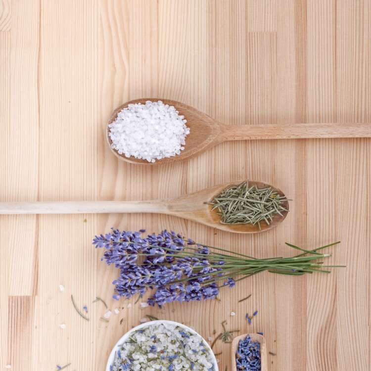 Auf einem Tisch liegt ein Bündel Lavendel und Holzlöffel mit verschiedenen Kräutern