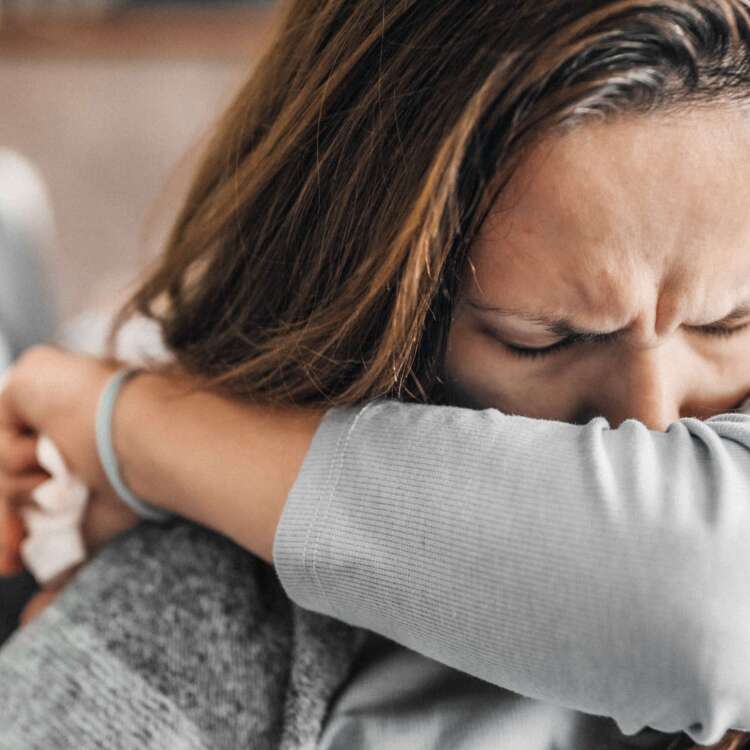 Frau mit Decke über der Schulter niest in die Armbeuge