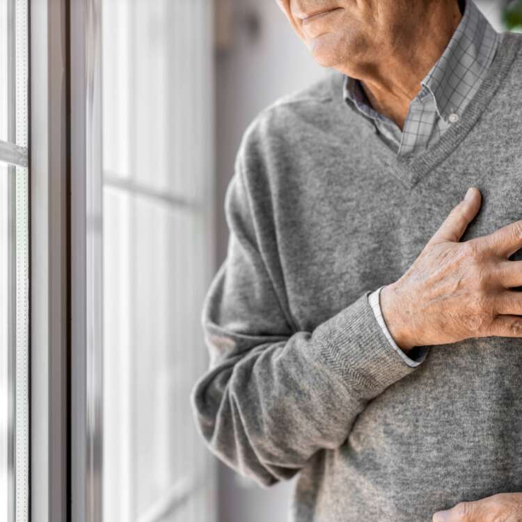 Eine Person steht am Fenster und hält sich die Brust