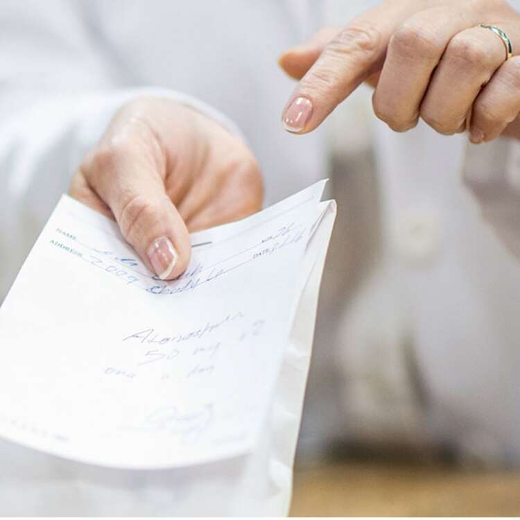 Eine Hand, welches ein Rezept für ein Medikament in der Hand hält und mit der anderen Hand darauf zeigt