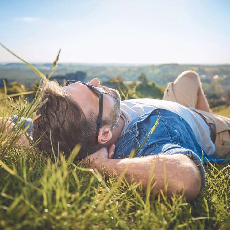 Eine Person liegt mit Sonnenbrille im Gras und geniesst die Sonne