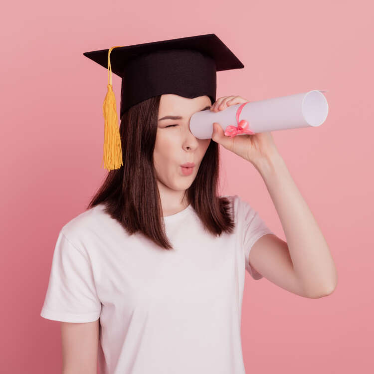 Eine junge Person mit Absolventenhut nutzt ihr Diplom als Fernrohr