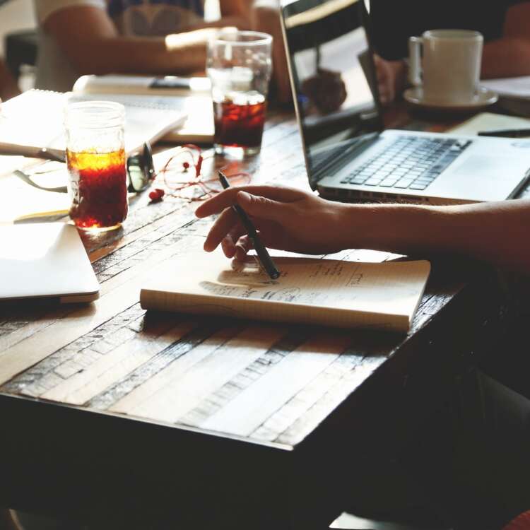Ein Schreibtisch, wo Leute am Notebook arbeiten oder sich Notizen machen