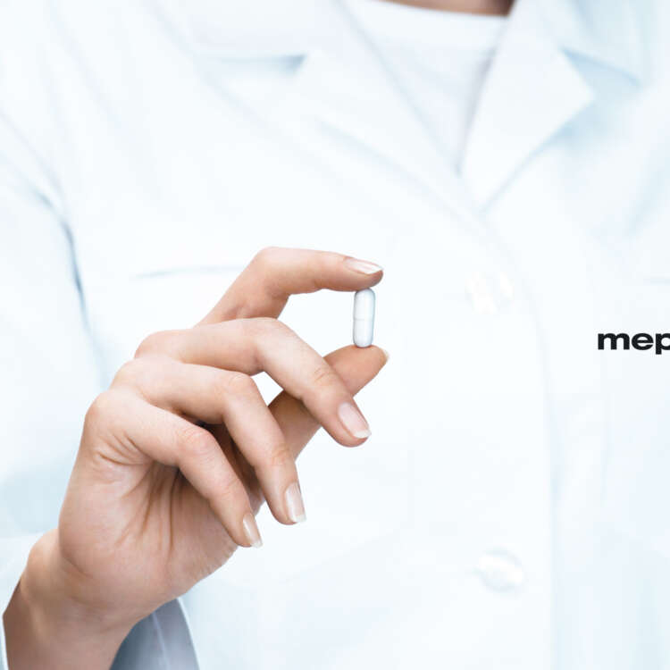 Eine Fachperson mit einem mepha-Kittel hält eine Pille